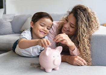 A parent helping their child put coins into a piggy bank