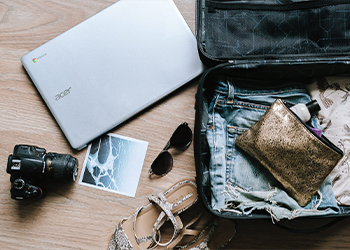 An open suitcase with clothes, shoes, sunglasses, a laptop, and a camera.